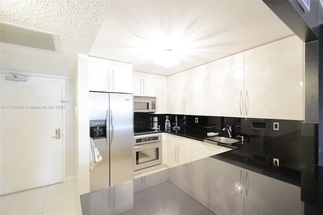 kitchen with white cabinets, sink, decorative backsplash, light tile patterned floors, and stainless steel appliances