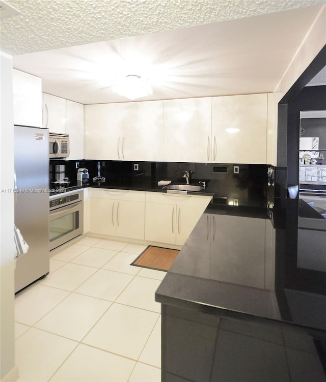 kitchen featuring white cabinetry, sink, backsplash, light tile patterned flooring, and appliances with stainless steel finishes