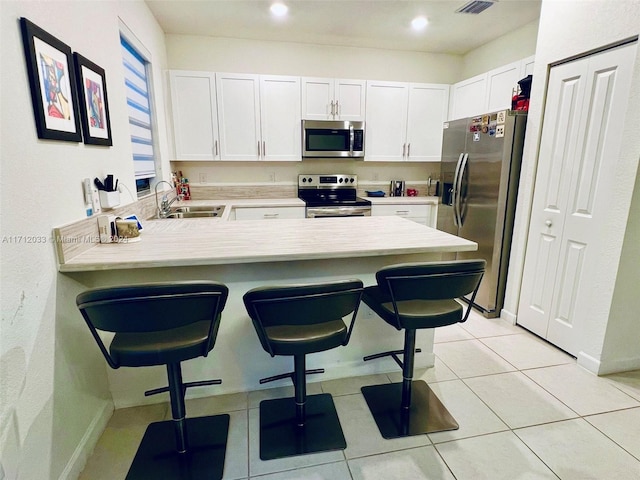 kitchen featuring white cabinetry, sink, kitchen peninsula, a kitchen bar, and appliances with stainless steel finishes