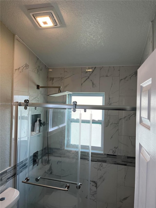 bathroom with a shower with shower door, toilet, and a textured ceiling