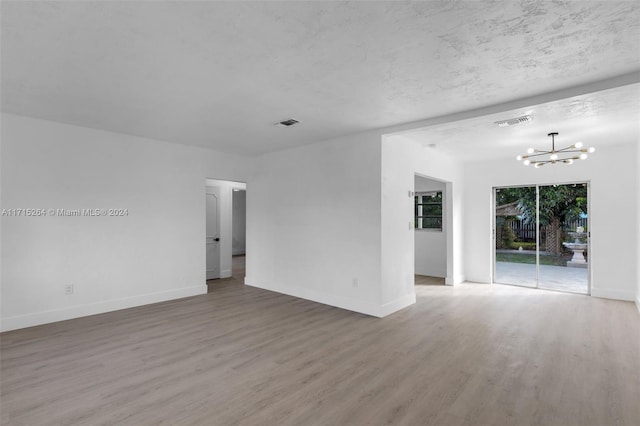 unfurnished room with hardwood / wood-style flooring, a textured ceiling, and an inviting chandelier