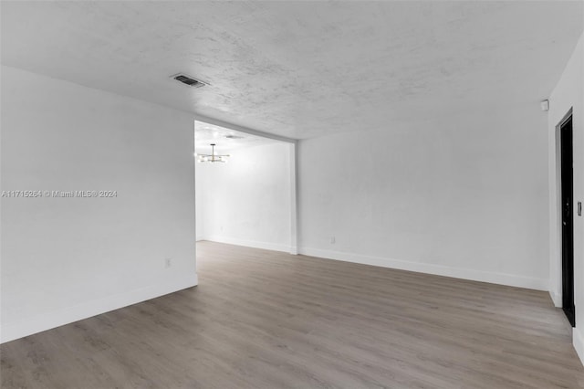 empty room featuring hardwood / wood-style floors, a notable chandelier, and a textured ceiling