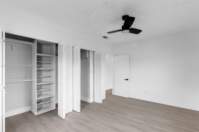 unfurnished bedroom featuring two closets, hardwood / wood-style flooring, and ceiling fan