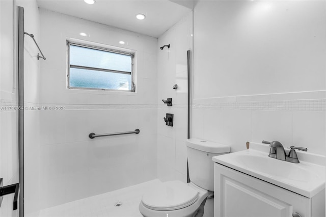 bathroom with vanity, toilet, tiled shower, and tile walls