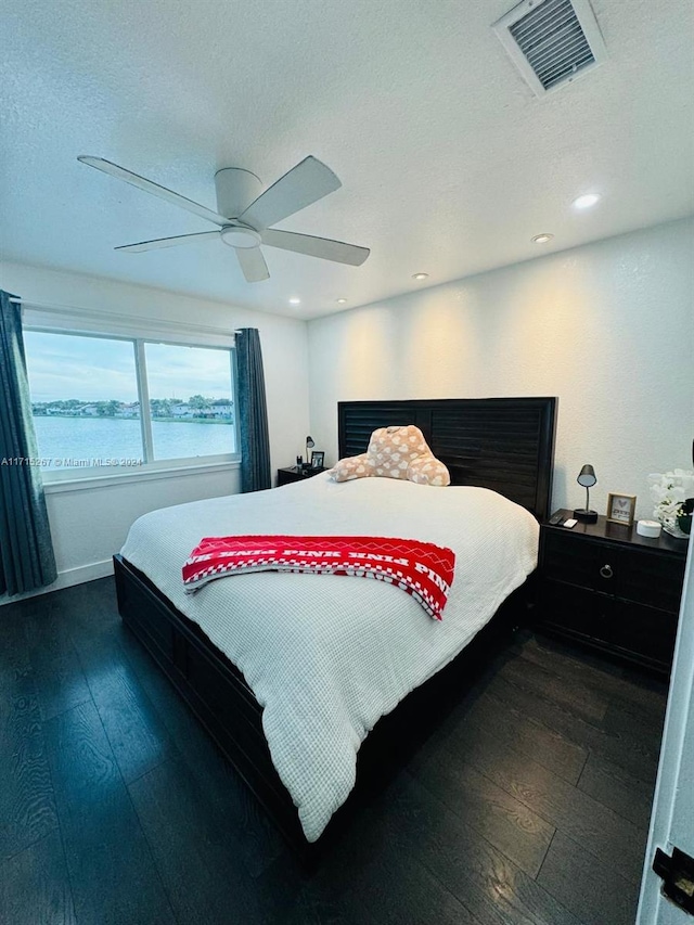 bedroom with a textured ceiling, a water view, ceiling fan, and dark hardwood / wood-style floors