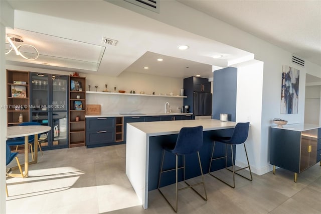 kitchen with kitchen peninsula, stainless steel fridge, a kitchen bar, and sink