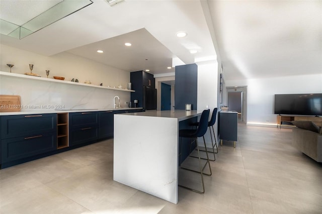 kitchen featuring black refrigerator, tasteful backsplash, sink, a center island, and a breakfast bar area