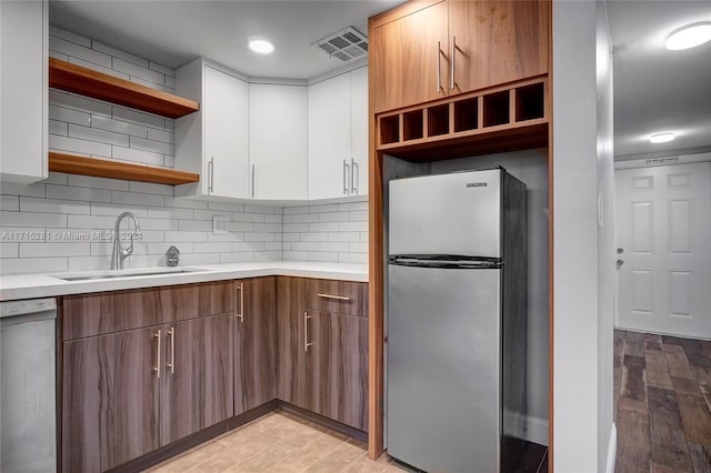 kitchen with stainless steel fridge, tasteful backsplash, sink, dishwasher, and white cabinets