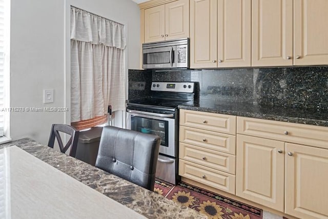 kitchen with decorative backsplash, stainless steel appliances, dark stone counters, and cream cabinets