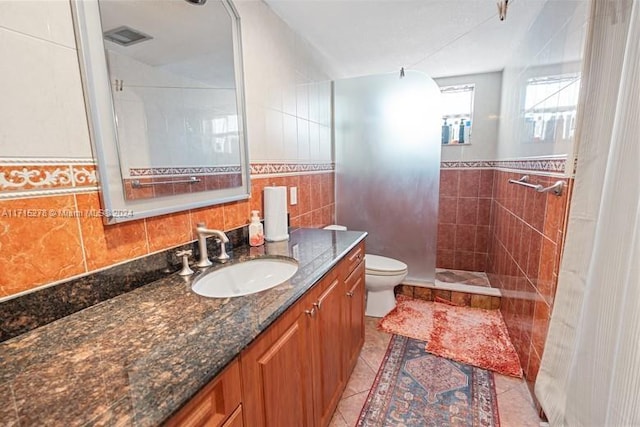 bathroom with tile patterned floors, a tile shower, vanity, tile walls, and toilet