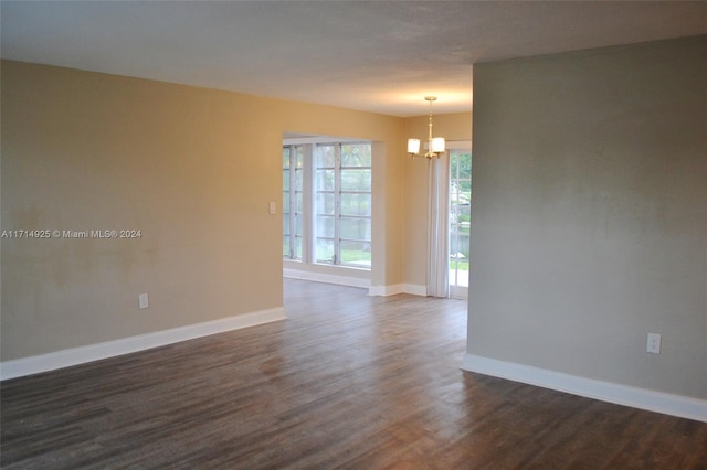 empty room featuring a notable chandelier and dark wood-type flooring