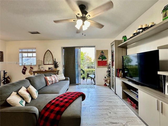 living room with a textured ceiling, light hardwood / wood-style floors, and ceiling fan