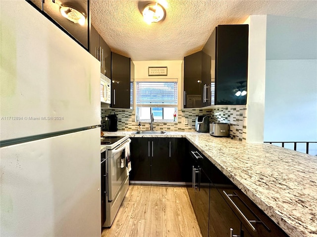 kitchen featuring light stone countertops, sink, backsplash, light hardwood / wood-style floors, and white appliances