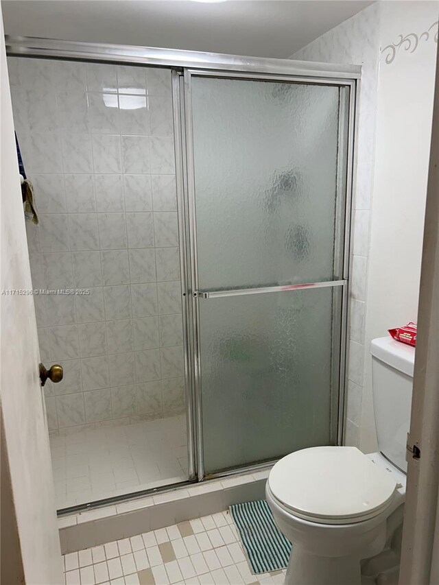 bathroom featuring tile patterned floors, toilet, and a shower with shower door