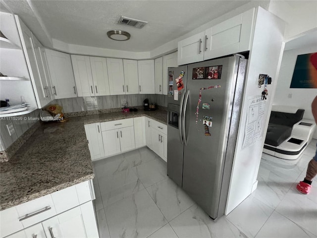 kitchen featuring stainless steel fridge, white cabinetry, and dark stone counters