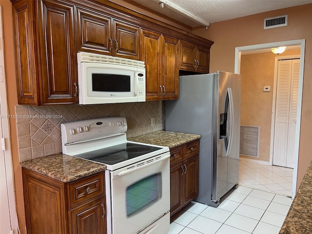 kitchen with decorative backsplash, white appliances, dark stone counters, and light tile patterned flooring