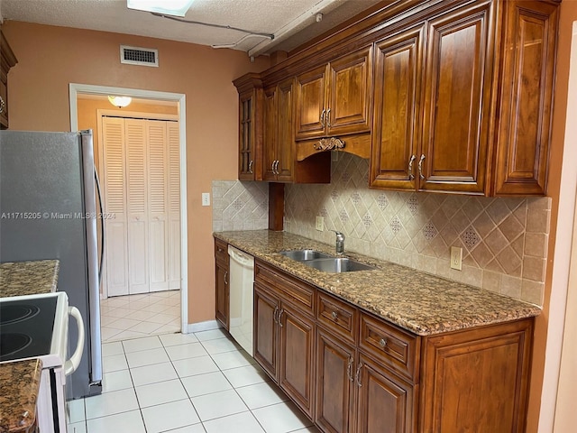 kitchen featuring dark stone counters, white dishwasher, sink, light tile patterned flooring, and range