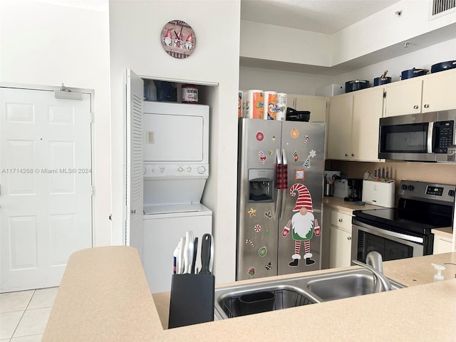 kitchen with light tile patterned flooring, stacked washing maching and dryer, sink, and appliances with stainless steel finishes