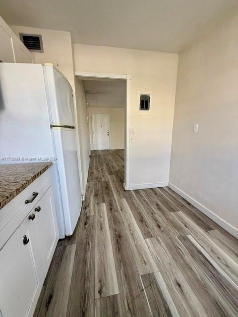 kitchen featuring white cabinetry, white fridge, light stone counters, and wood-type flooring