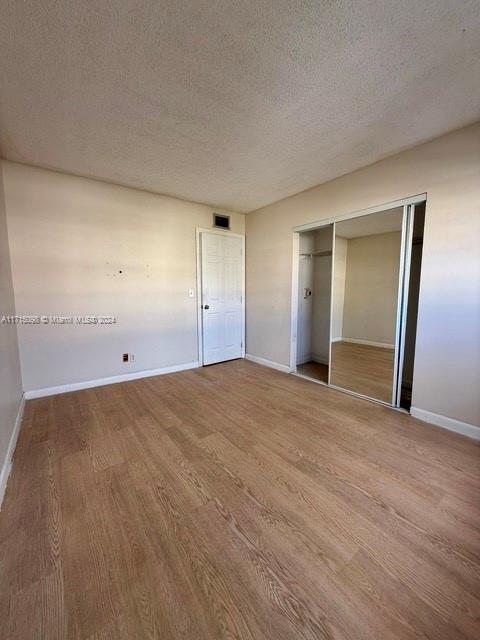 unfurnished bedroom featuring a closet, wood-type flooring, and a textured ceiling