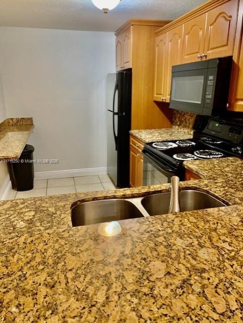 kitchen with light tile patterned floors, sink, light stone counters, and black appliances