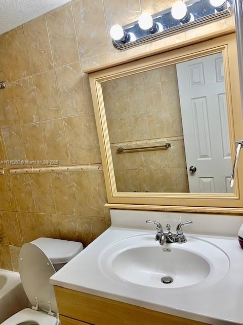 bathroom with vanity, a textured ceiling, toilet, and tile walls