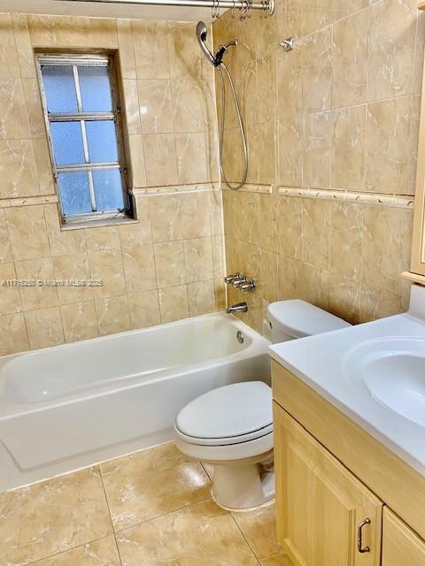 full bathroom featuring tile patterned floors, toilet, vanity, tile walls, and tiled shower / bath