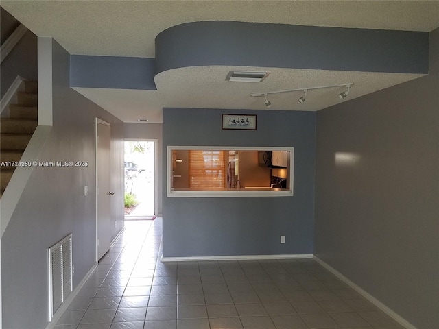 hall featuring tile patterned flooring, a textured ceiling, and track lighting