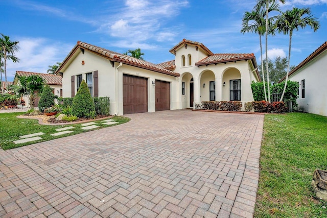 mediterranean / spanish home featuring stucco siding, an attached garage, a tile roof, and decorative driveway