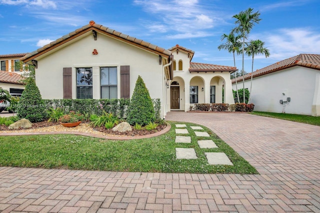 mediterranean / spanish-style house with a tile roof, decorative driveway, and stucco siding