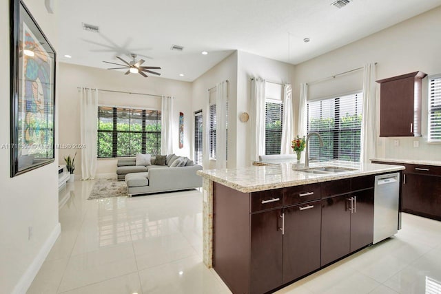 kitchen with stainless steel dishwasher, dark brown cabinets, sink, light tile patterned floors, and a center island with sink