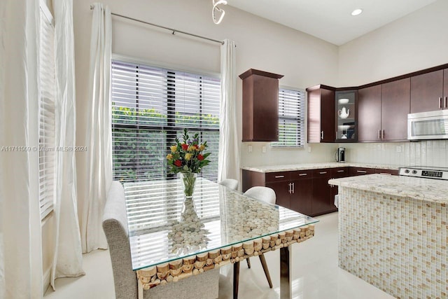 kitchen with light stone countertops, backsplash, stove, dark brown cabinets, and light tile patterned floors