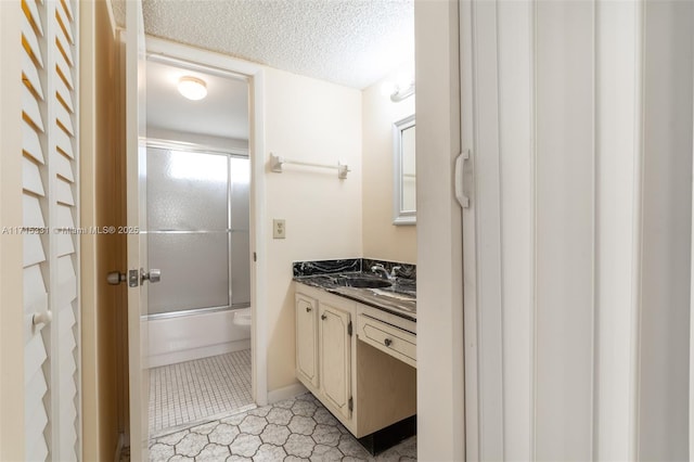 bathroom with a textured ceiling, vanity, and bath / shower combo with glass door