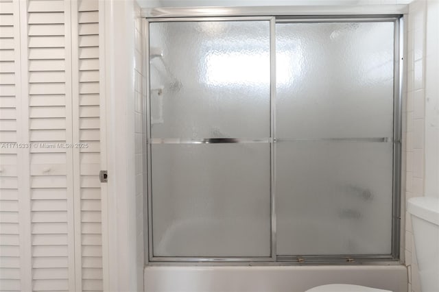 bathroom with toilet and shower / bath combination with glass door