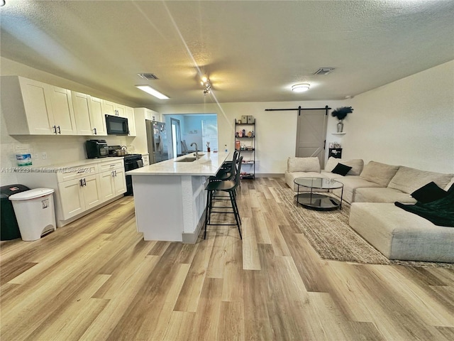 kitchen with a barn door, an island with sink, white cabinetry, and black appliances