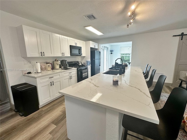 kitchen with light stone countertops, sink, black appliances, a barn door, and white cabinets