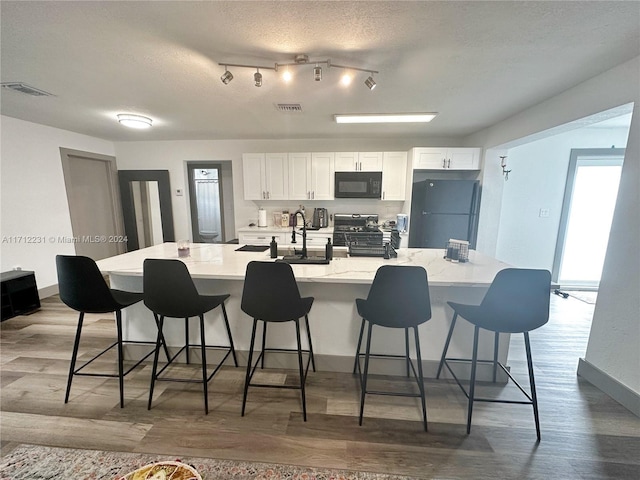 kitchen featuring black appliances, a spacious island, a textured ceiling, white cabinetry, and a breakfast bar area