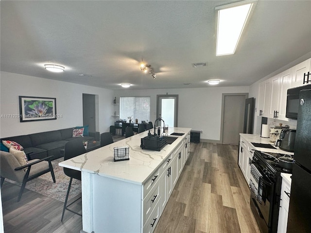 kitchen with a kitchen breakfast bar, light stone counters, black appliances, a center island with sink, and white cabinets