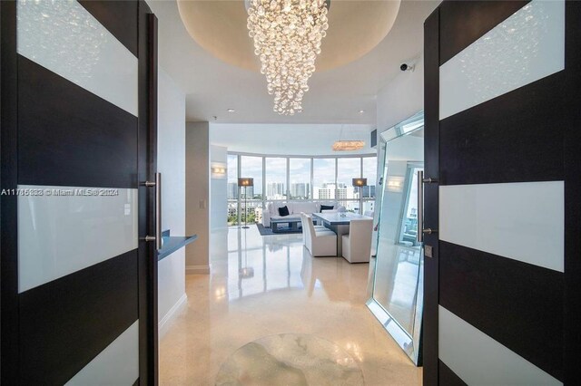 hallway with a tray ceiling, floor to ceiling windows, and a notable chandelier