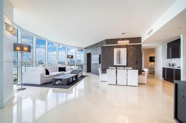 living room featuring a chandelier, wood walls, a healthy amount of sunlight, and a wall of windows