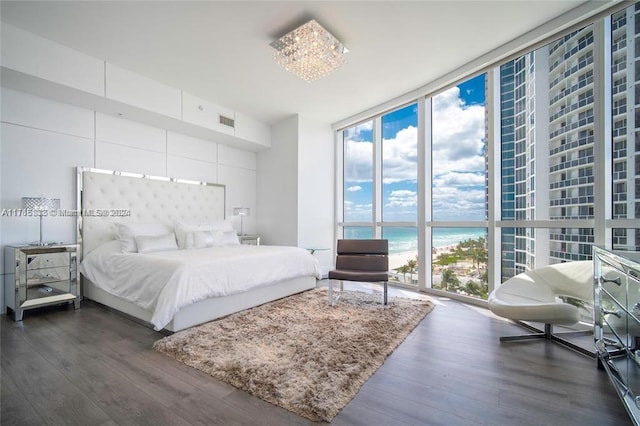 bedroom featuring a notable chandelier, floor to ceiling windows, a water view, and dark wood-type flooring