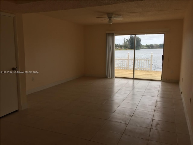 empty room with ceiling fan, light tile patterned flooring, and a water view