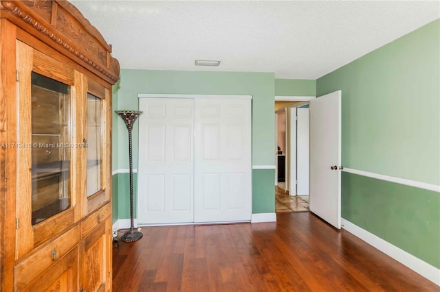 unfurnished bedroom featuring a textured ceiling, dark hardwood / wood-style floors, and a closet