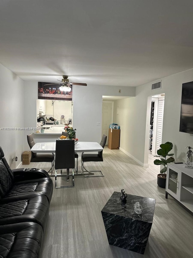 living room with a ceiling fan, visible vents, baseboards, and wood finished floors