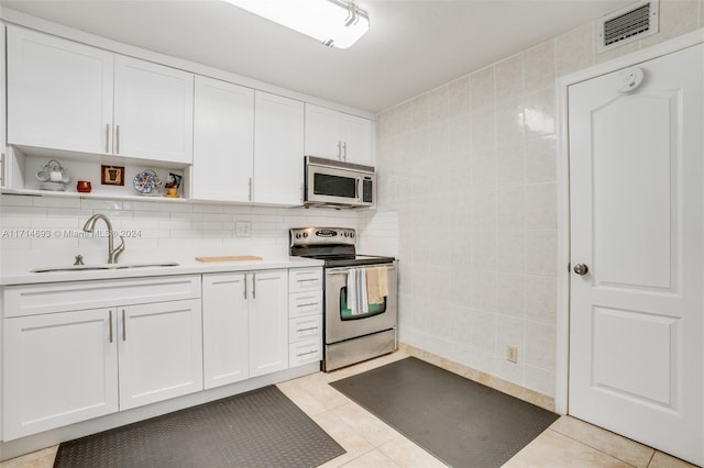 kitchen featuring appliances with stainless steel finishes, white cabinetry, light tile patterned floors, and sink