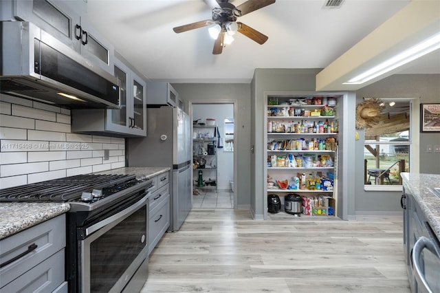 kitchen with light stone counters, appliances with stainless steel finishes, light hardwood / wood-style flooring, and backsplash