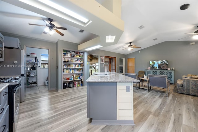 kitchen with sink, stainless steel stove, lofted ceiling with skylight, a center island with sink, and light wood-type flooring