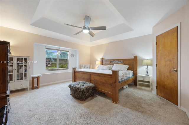 bedroom featuring ceiling fan, light colored carpet, and a tray ceiling