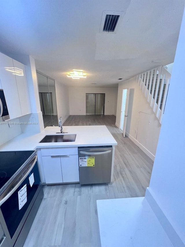 kitchen featuring white cabinets, sink, light wood-type flooring, a textured ceiling, and stainless steel appliances