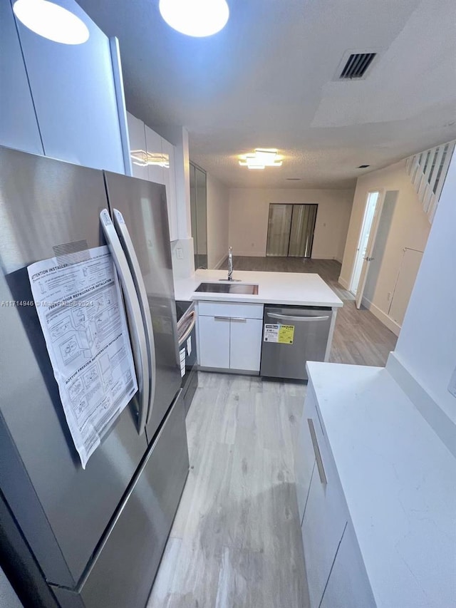 kitchen with white cabinets, light wood-type flooring, sink, and appliances with stainless steel finishes